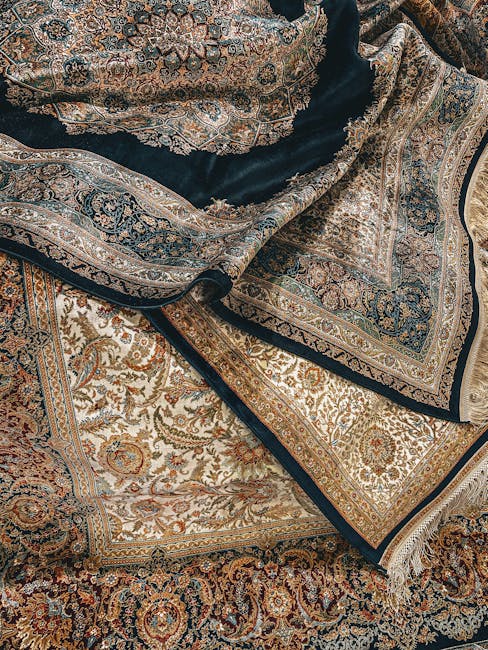Close-up view of a traditional patterned area rug with intricate floral and geometric designs in red, cream, blue, and orange hues, partially rolled back to reveal a dark, polished wooden floor underneath. The rug has fringed edges, and the area appears well-maintained and clean. The room is lit with natural light casting a shadow across the floor and the rug. The scene suggests a focus on surface cleaning and rug restoration, with the professional cleaning company Harrow Carpet Cleaning specializing in detailed fabric and surface hygiene within a domestic setting.